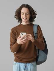 Young handsome man with backpack looking at smart phone over gray background. Smiling student going on travel	 - 746317761