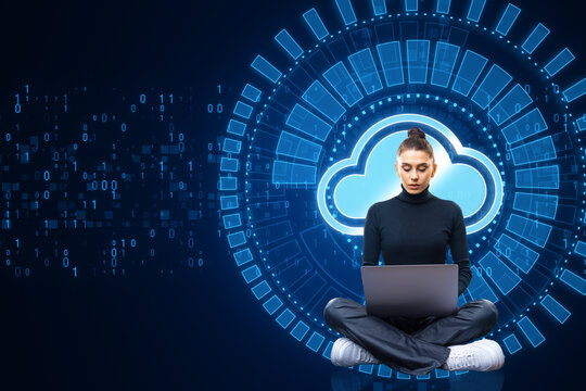 Attractive young european woman using laptop while sitting with creative glowing cloud computing hologram with binary coding on dark blue background. Digital server, support and network concept.