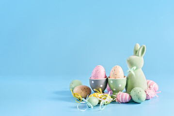 Happy Easter greeting card. soft pastel green Easter bunny figurine and collection of colorful, decorated Easter eggs against a vibrant blue background. - 746324787