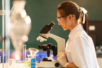 Side view of Asian female scientist Use a microscope to smile and research cells for making...