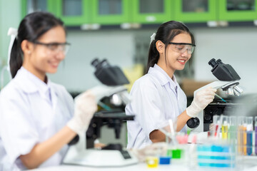 2 Asian female scientists Use a microscope to research chemical cells for the business industry, pharmaceutical companies and hospitals, making vaccines for medical use to treat patients.