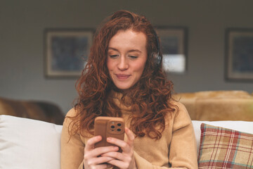 Happy young redhead woman in brown shirt and using a mobile phone, listening to favorite songs,...