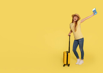 Happy redhead woman in yellow t-shirt with a suitcase and passport with tickets sitting and going to a journey on a yellow background. Travel concept