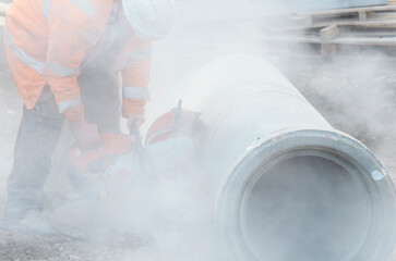 Construction worker cutting concrete pipe for drainage using a cut-off saw. Cutting concrete with a...