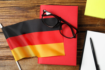Learning foreign language. Flag of Germany, book, glasses and stationery on wooden table, flat lay