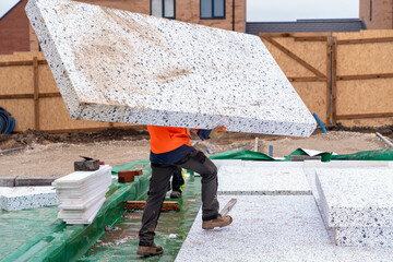 Builder placing polystyrene insulation boards on waterproofing membrane during floor construction. Energy saving concept