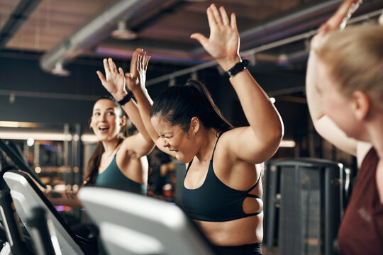 Ecstatic group of fit young women in sportswear laughing and high-fiving each other after a cardio workout session on stationary bikes in a gym