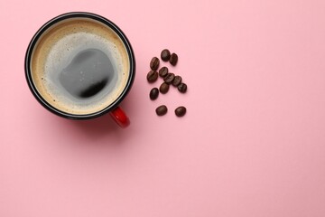 Fresh coffee in cup and roasted beans on pink background, top view. Space for text