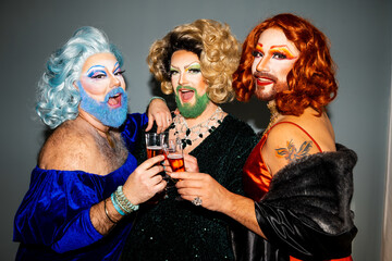 Three glamorous drag queens toasting with champagne at a festive gathering