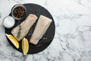 Fresh raw cod fillets, spices and lemon on white marble table, top view