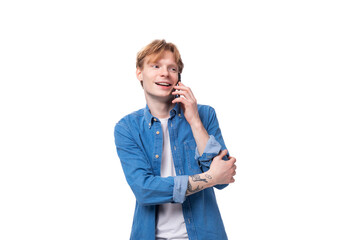 portrait of a smiling caucasian red-haired guy in a denim blue shirt chatting on the phone