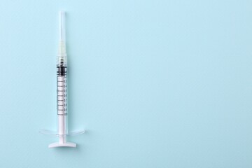 Cosmetology. Medical syringe on light blue background, top view. Space for text