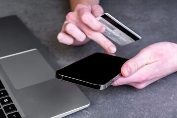 Hands holding smartphone and using credit card for online shopping.
