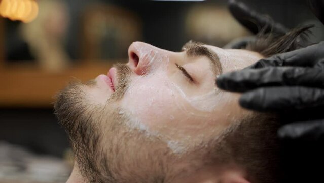 Man receives relaxing facial massage at barbershop spa. Professional beautician performs skincare routine, rejuvenating clients face. Grooming session, male wellness, luxury treatment depicted.