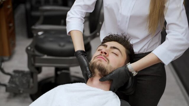 Professional gives relaxing facial massage to man at barbershop. Gentle skin care, beard grooming. Client enjoys expert treatment, luxury salon setting. Masculine wellness, pampering closeup.