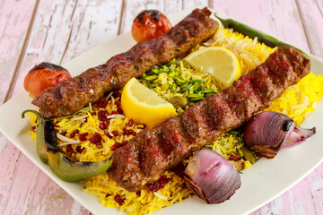Chelo Kabab Rice topping with pistachio, onion, tomato, lemon slice and pomegranate seeds served in dish isolated on table closeup top vie of arabic spicy food