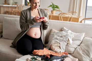 Pregnant woman taking pictures of baby clothes