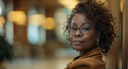 Fotobehang Confident black senior businesswoman in a stylish blazer and glasses, emanating experience and wisdom. Leadership, experience in the workplace, and the dignified aging of professional women. © radekcho