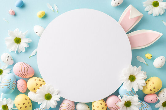 Easter magic setup. Top view image of rainbow-hued eggs, and fragrant spring flora on a pastel blue background, with sweet rabbit ears showing through a free area for loving greetings or advertising