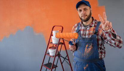Adult bearded painter man in blue overalls over orange wall background celebrating win showing sign...