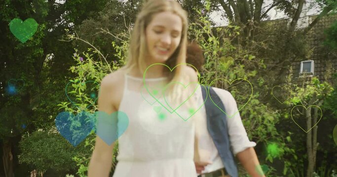 Animation of colourful hearts over happy walking in garden on wedding day