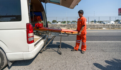 Asian rescue staff in orange uniform stand next to an ambulance pulling a stretcher out of an...