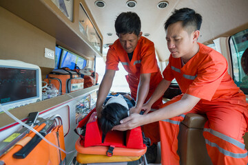 Two paramedics in orange uniforms are helping a patient inside an ambulance.