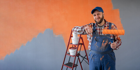 Young painter caucasian man holding roller on orange wall background showing thumb down with negative expression - obrazy, fototapety, plakaty