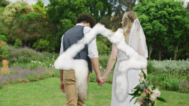 Animation of cloud house over happy diverse couple walking in garden on wedding day