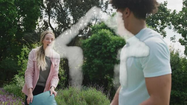 Animation of cloud house over happy diverse couple having pillow fight in garden