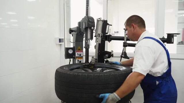 Auto mechanic uses tire changer machine workshop seasonal wheel rotation. Expert replaces car tires, ensuring vehicle safety, prep for winter driving conditions. Professional service, garage work.