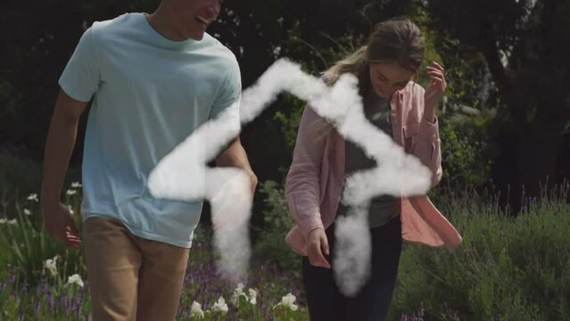 Animation of cloud house over happy diverse couple dancing and holding hands in garden