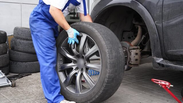 Auto mechanic installs tire on vehicle using air wrench at service station. Worker fastens lug nuts, aligns wheel, ensures car safety. Garage pro replaces rim, conducts maintenance.