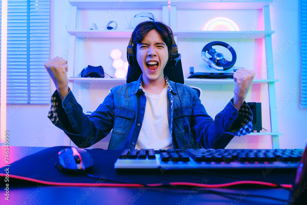 Wall mural portrait of asian male gamer celebrating victory in front of the gaming table. gamer winning an espo