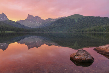 Ideal pink sunset on the banks of the lake in the mountains scenery. Stones in the water,...