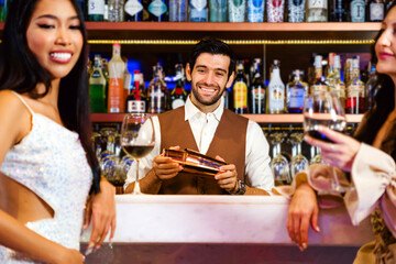 Caucasian professional bartender or mixologist making a cocktail for women at a bar. Attractive...