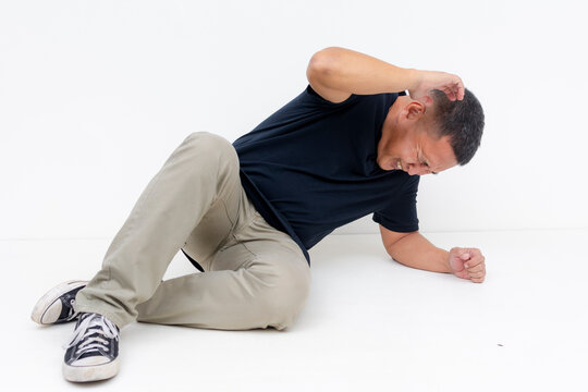 A scared middle aged Asian man drops on the ground cowering and frozen in fear with a defensive posture.