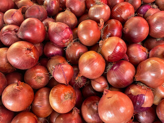 Pile of Unpeeled Red Onions.Lots of raw onions stacked on top of each other. View from above.Organic and fresh onions are just harvested and ready for sale. Healthy eating.Images of vegetable products