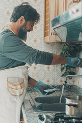 Husband one man washing dishes at home alone smiling and enjoying cleaning housekeeping indoor...