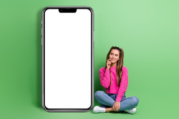 Full length photo of minded woman dressed pink sweater sit look at smartphone screen empty space isolated on green color background