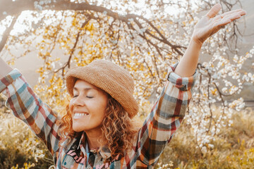 Springtime. Welcome spring concept image with overjoyed happy woman raising arms and closing eyes hugging and loving nature around. Outdoor people leisure activity concept. Freedom and success day - obrazy, fototapety, plakaty