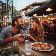 Foto op Canvas Happy young adult couple have fun eating a pizza together outdoor in traditional italian pizzeria restaurant sitting and talking and laughing. People enjoying food and dating relationship. Tourists © simona
