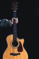 Acoustic guitar in a male hand on a black background.