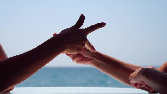Rock paper scissors being played by two young woman. Close up view female hands playing stone, scissors and paper on sea background, funny carefree game. Friendship, dealing with conflict, having fun.