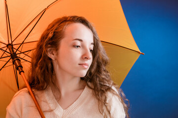 Portrait of a pensive pretty girl under a yellow umbrella in front of a dark blue background - 746359949