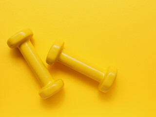 Two yellow dumbbells on a yellow background