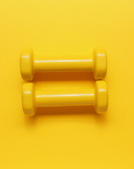Two yellow dumbbells on a yellow background
