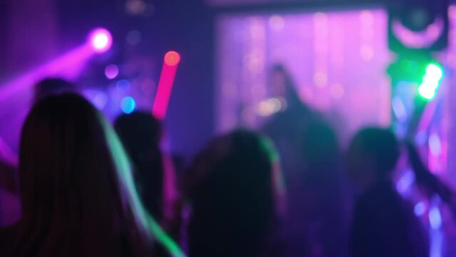 People dance to the music of a DJ in a nightclub. Blurred video.