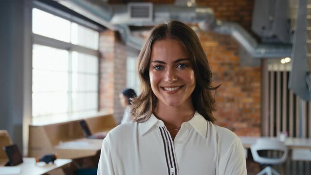 Portrait of smiling young businesswoman working in modern open plan office turning to look at camera - shot in slow motion
