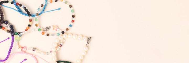 Banner with handmade bracelets made of beads and cords on a beige background. - obrazy, fototapety, plakaty